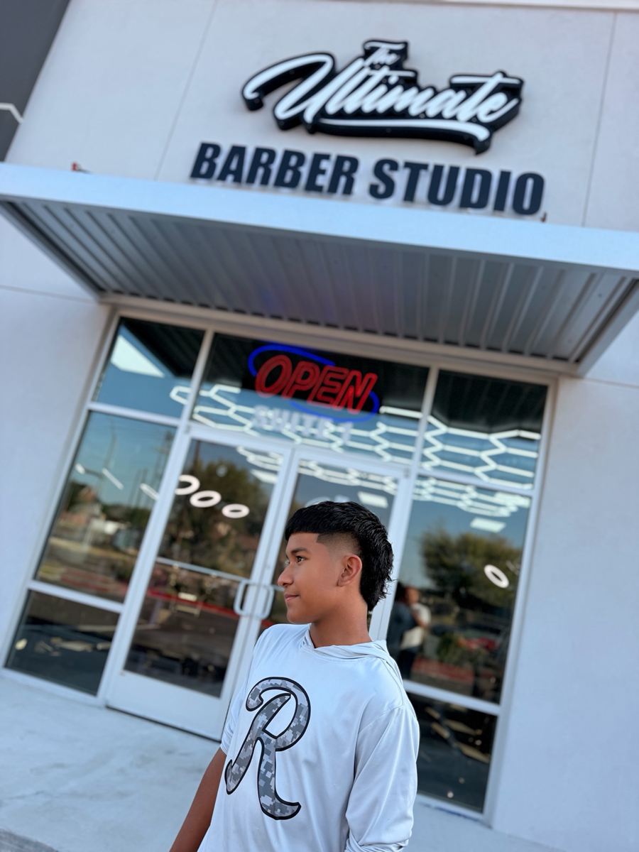Client with a burst fade mullet standing under The Ultimate Barber Studio sign
